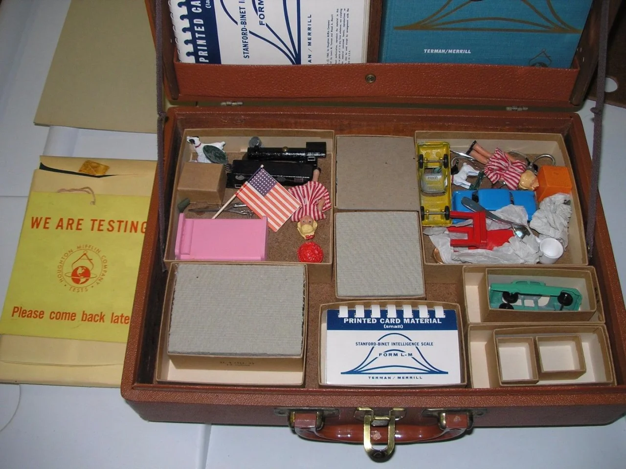 A Stanford-Binet Form L-M test kit from c. 1960 — printed cards, miniature toys, and Terman/Merrill manuals laid out in a small case.